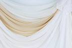 a close-up view of a white and beige fabric, possibly a curtain or drape, with a soft, flowing texture.