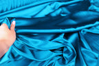 A hand is holding a piece of blue satin fabric, which appears to be a close-up view of the material.