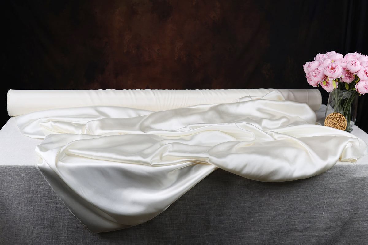 a white satin fabric draped over a gray tablecloth, with a vase of pink flowers placed next to it.