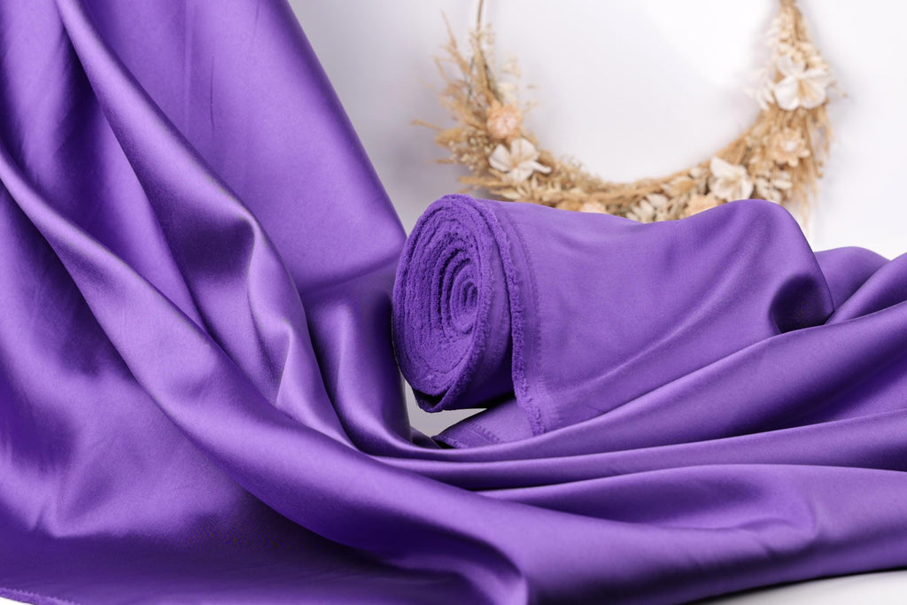 a close-up view of a purple satin fabric, with a wreath of dried flowers in the background.