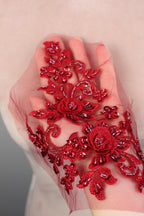 A hand adorned with a delicate red lace or embroidery, featuring intricate floral and leaf designs.