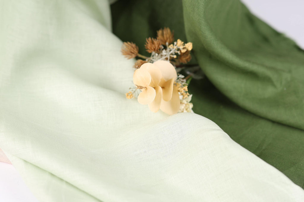 A close-up view of a delicate white flower resting on a green fabric, with the flower's petals gently curled and the leaves appearing slightly curled as well.