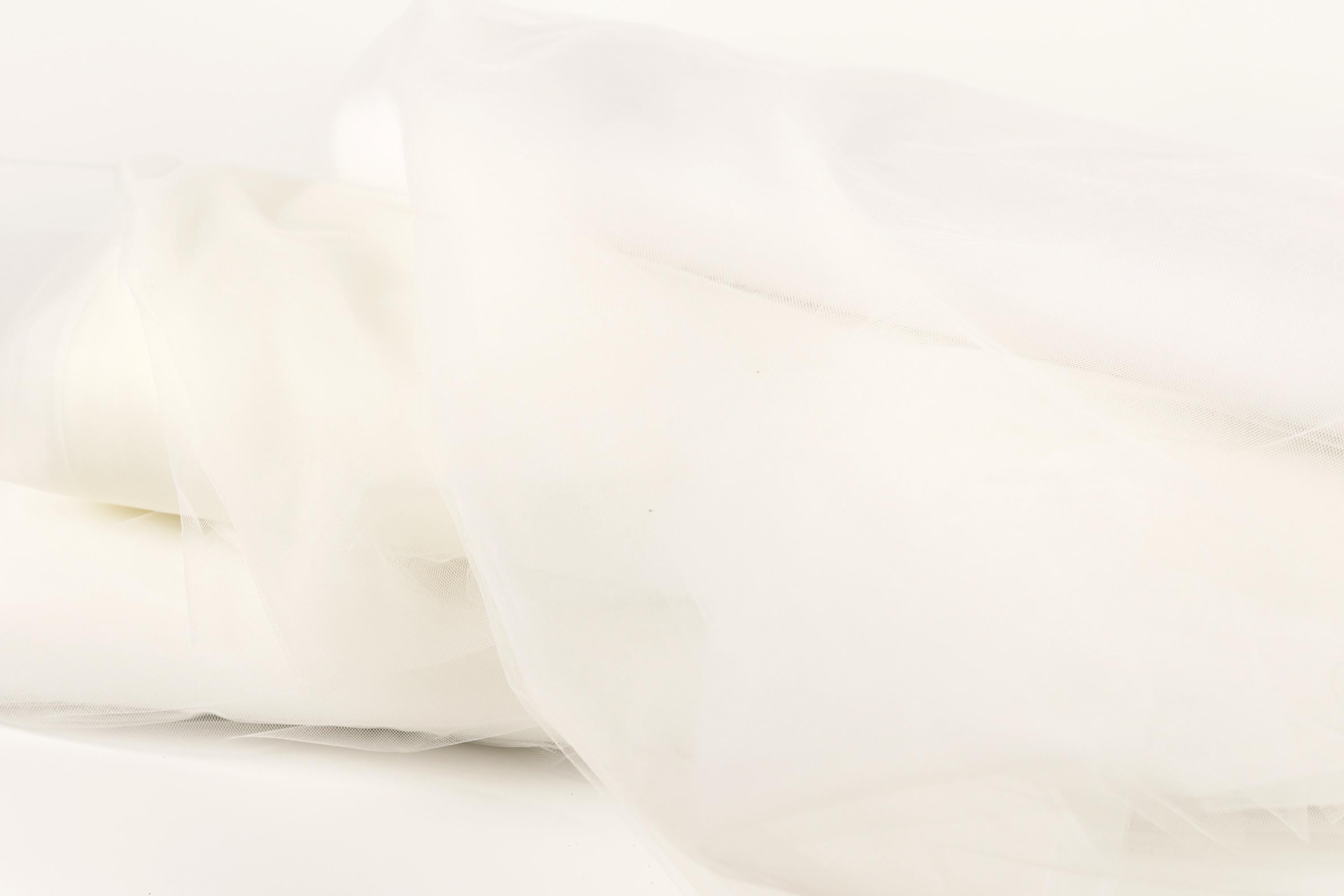 The image is a close-up of a white fabric, possibly a sheer or sheer-like material, with a soft, flowing texture.