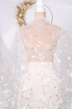 A mannequin wearing a white dress with a sheer, floral-patterned fabric draped over it.