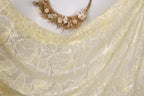 a close-up view of a delicate, yellow fabric with a floral pattern. The fabric appears to be made of sheer material, with a delicate and intricate design. The background is plain white, allowing the fabric and floral pattern to stand out prominently.