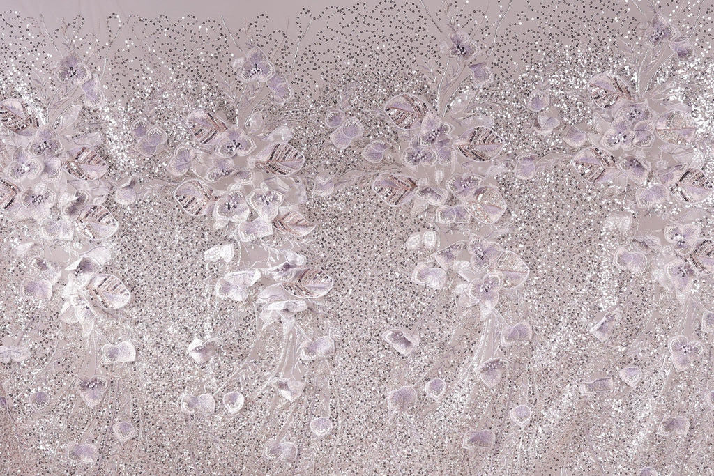 a close-up view of a fabric with a floral pattern, including white and purple flowers and leaves. The fabric appears to be made of a shiny, glittery material, giving it a sparkling and elegant appearance.
