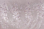 a close-up view of a fabric with a floral pattern, including white and purple flowers and leaves. The fabric appears to be made of a shiny, glittery material, giving it a sparkling and elegant appearance.