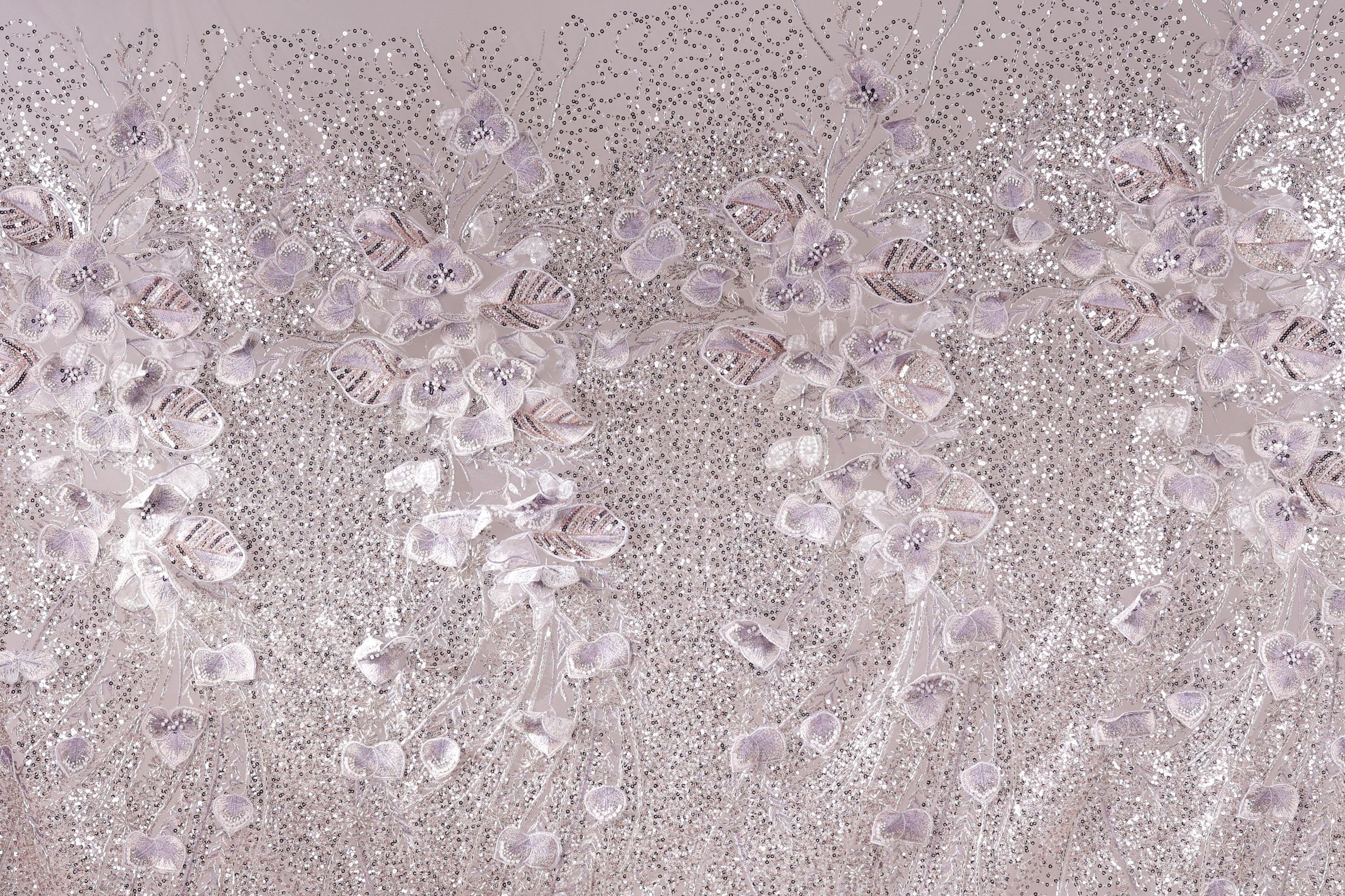 a close-up view of a fabric with a floral pattern, including white and purple flowers and leaves. The fabric appears to be made of a shiny, glittery material, giving it a sparkling and elegant appearance.