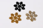 three glittery snowflake decorations of different sizes and colors against a white background.