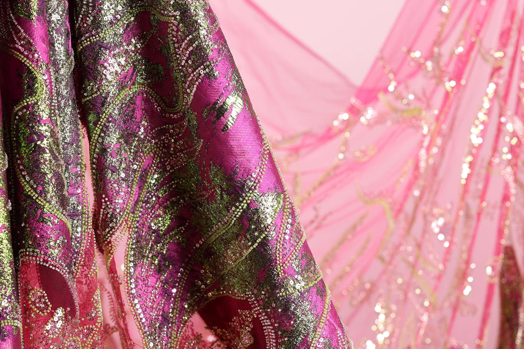 a close-up view of a fabric with a pink and green pattern, featuring a metallic or sequined texture.