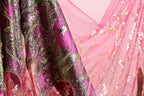 a close-up view of a fabric with a pink and green pattern, featuring a metallic or sequined texture.