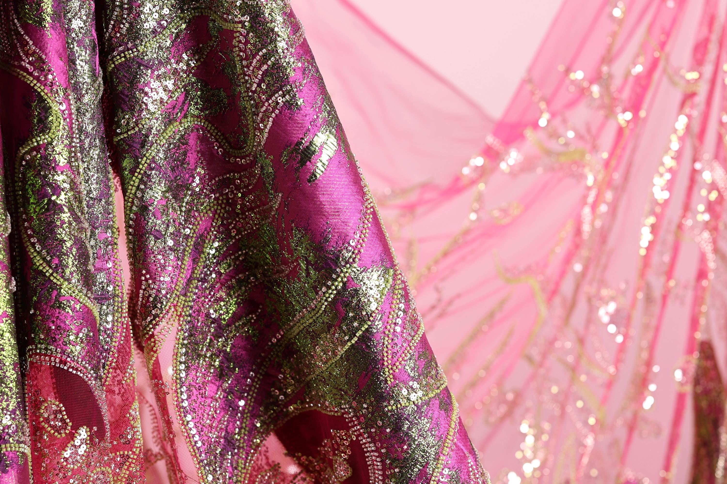 a close-up view of a fabric with a pink and green pattern, featuring a metallic or sequined texture.
