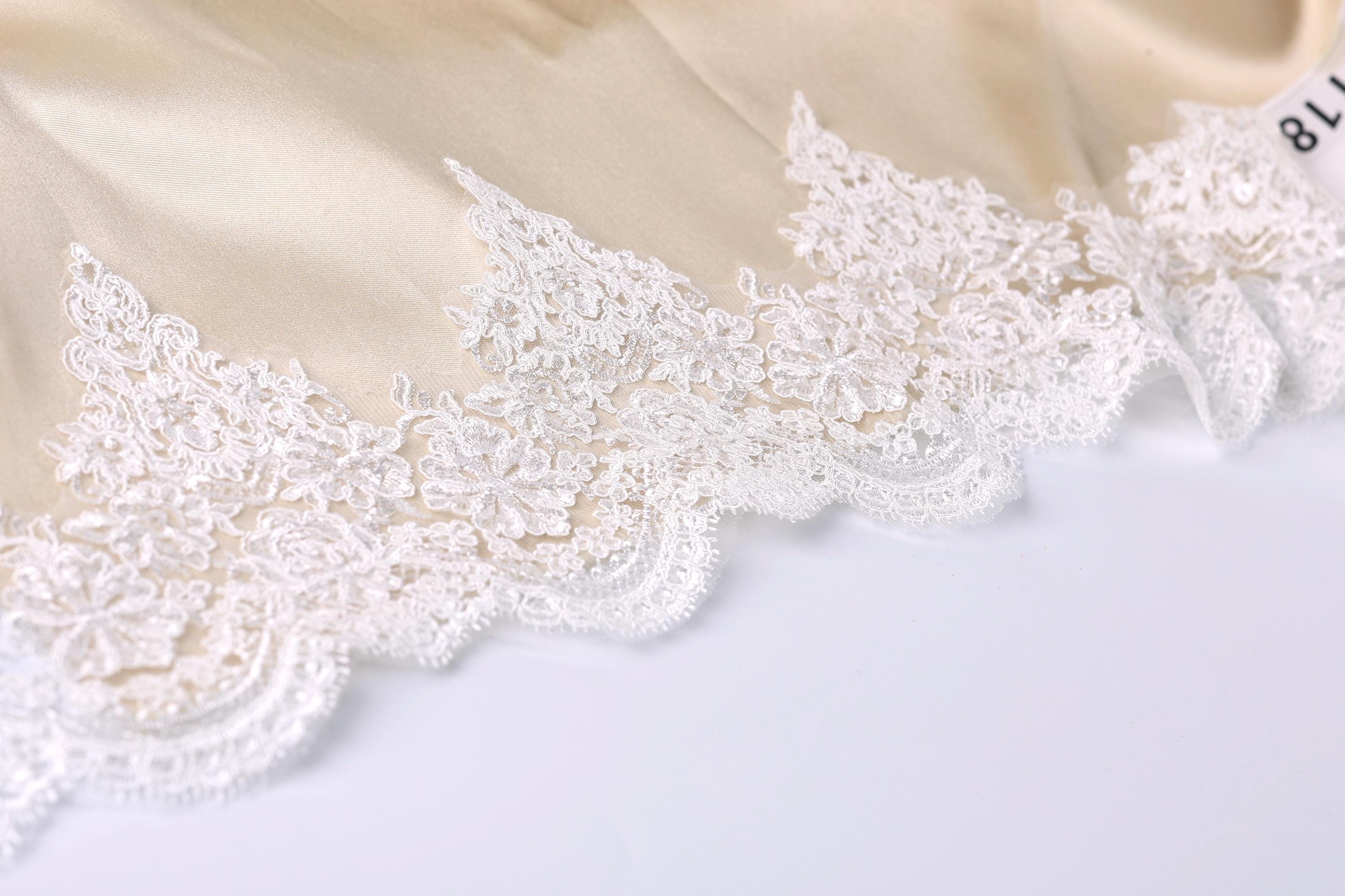 A close-up view of a delicate, white lace trim on a fabric, with intricate patterns and designs.