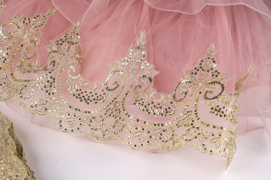 a close-up view of a delicate, pink tulle skirt with intricate gold embroidery and sequins.