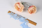 a pair of pink roses, a blue lace piece, and a wooden ruler on a white background.