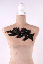 A mannequin with a beige body and a white headpiece, featuring a black lace-like design with small white beads or sequins.