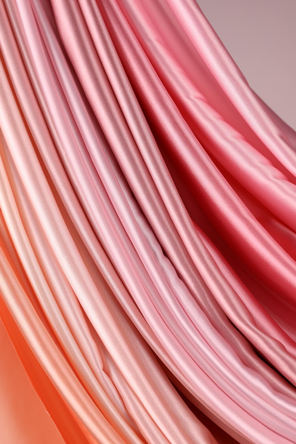 a close-up view of a soft, flowing fabric with a gradient of pink and orange colors. The fabric appears to be made of silk or satin, and it is arranged in a way that creates a sense of movement and texture. The colors are vibrant and the fabric looks delicate and luxurious.