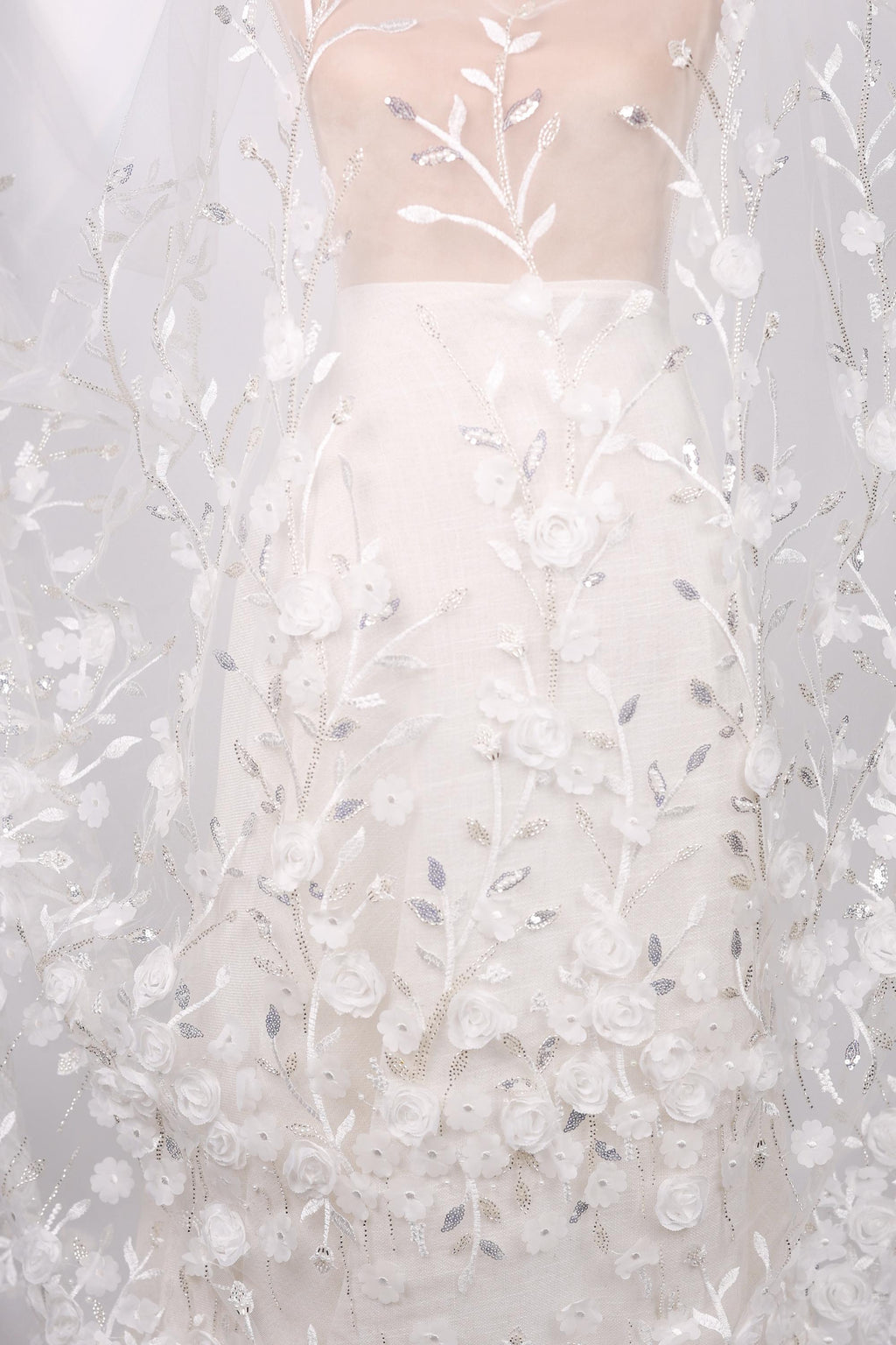 a white dress with a floral pattern, including white flowers and leaves. The dress appears to be made of a sheer fabric, giving it a delicate and elegant appearance.