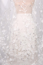 a white dress with a floral pattern, including white flowers and leaves. The dress appears to be made of a sheer fabric, giving it a delicate and elegant appearance.