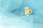 A delicate arrangement of yellow flowers rests on a light blue fabric, creating a serene and calming visual.