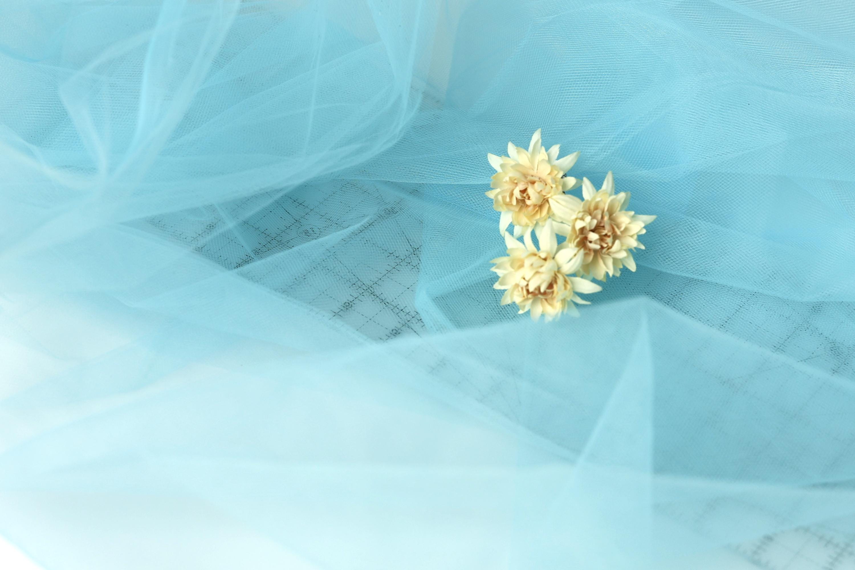 A delicate arrangement of yellow flowers rests on a light blue fabric, creating a serene and calming visual.