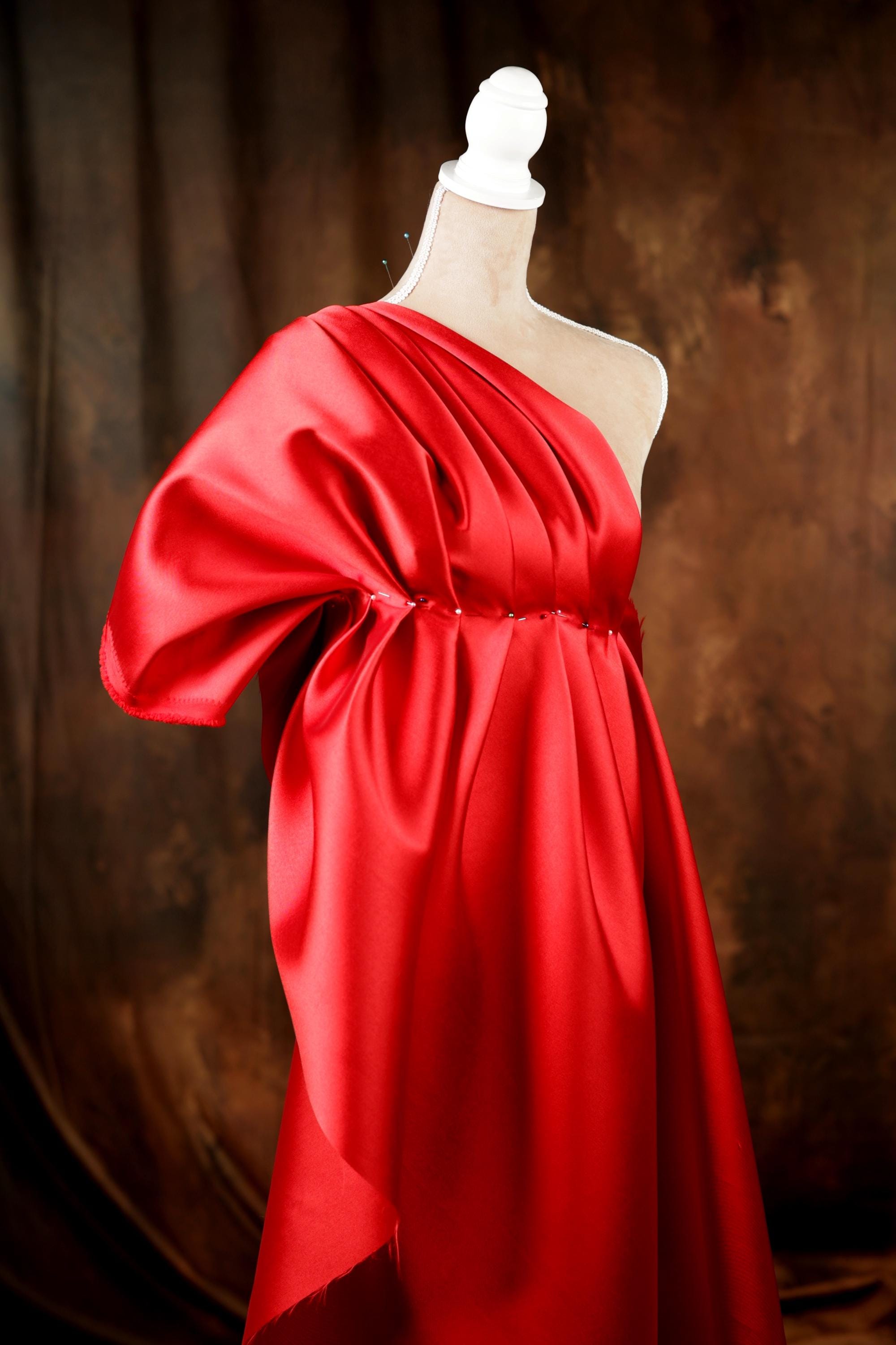 A mannequin wearing a vibrant red one-shoulder dress with a flowing, draped design.