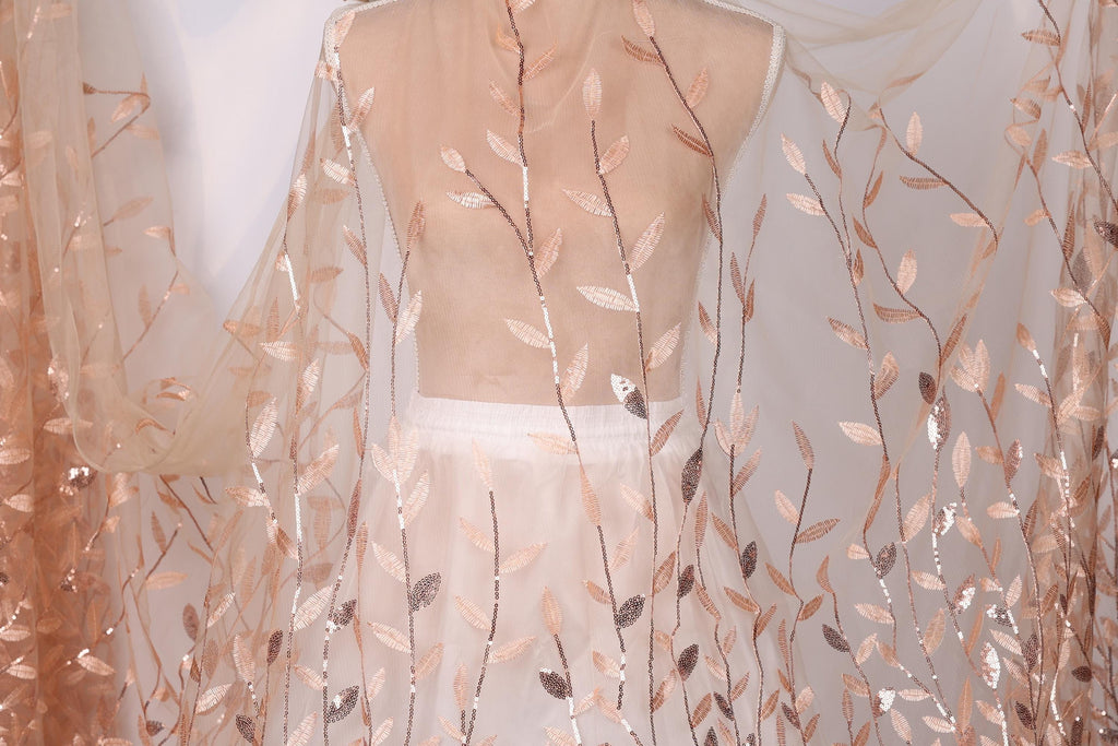 a mannequin wearing a white dress with a sheer, leaf-like fabric draped over it. The fabric has a delicate, floral pattern in shades of peach and white.
