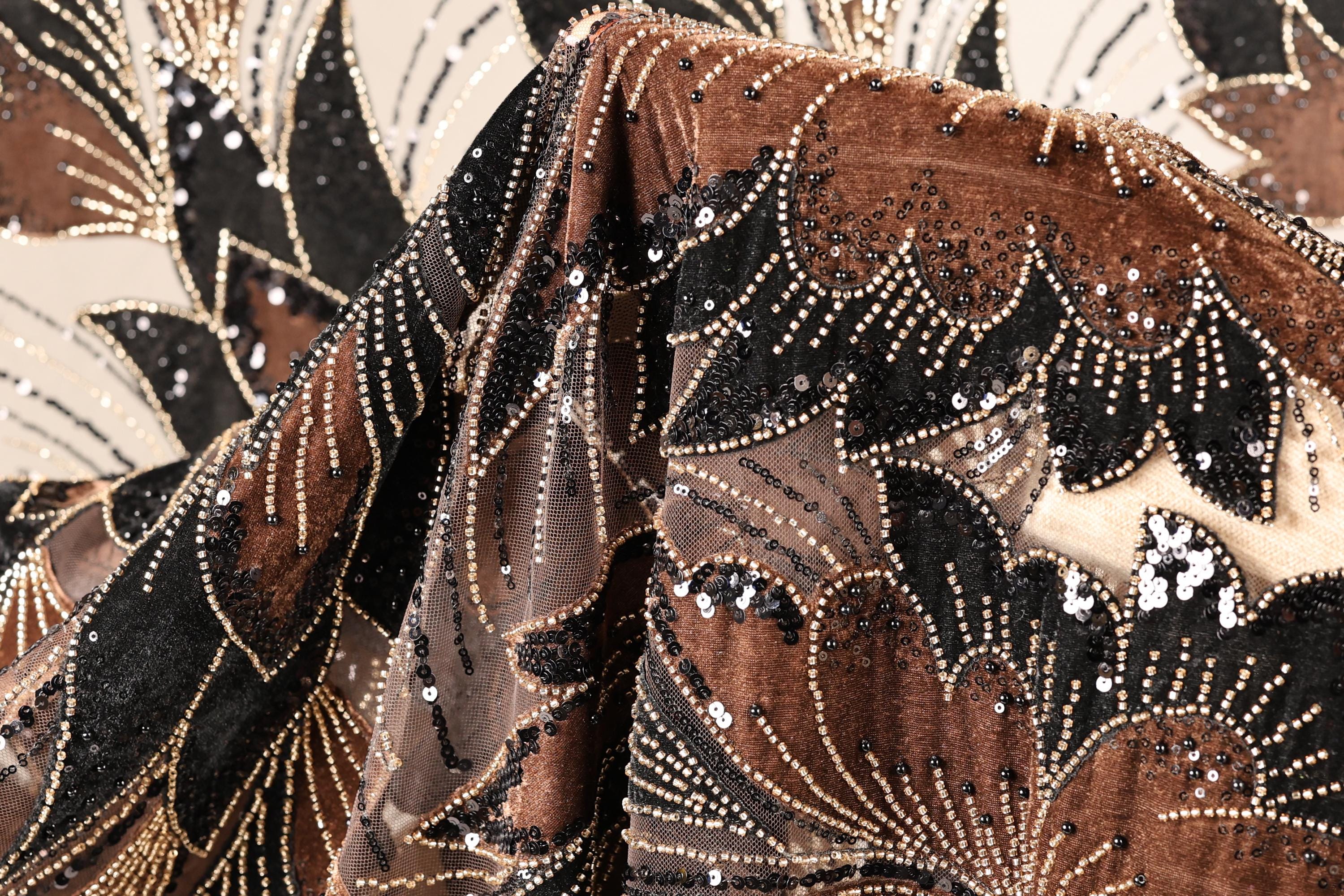 a close-up view of a fabric with a floral pattern and beaded designs in shades of brown and black.