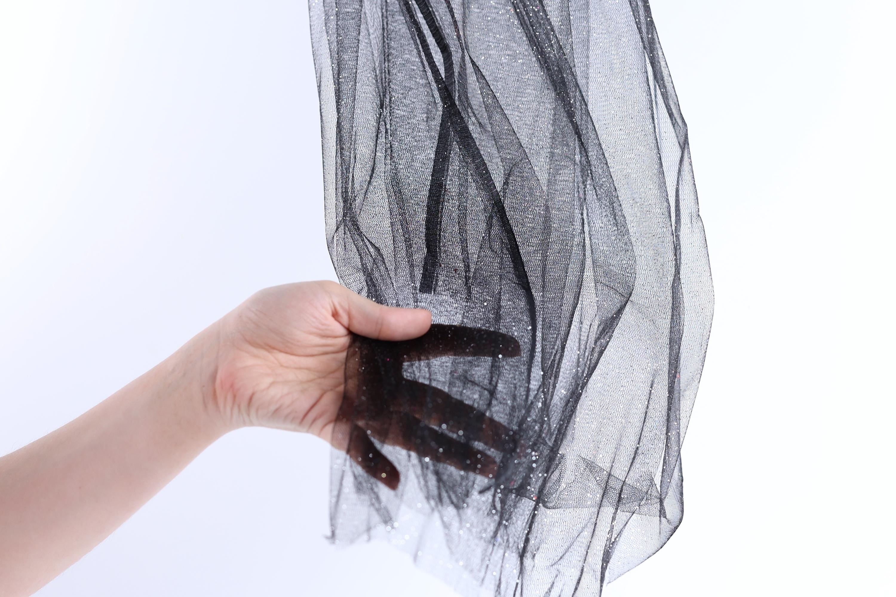 A hand is holding a black, shiny, and textured fabric, which appears to be a piece of sheer material or a decorative textile.