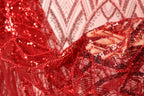 A close-up view of a hand holding a piece of red sequin fabric, with the fabric's intricate patterns and textures visible.