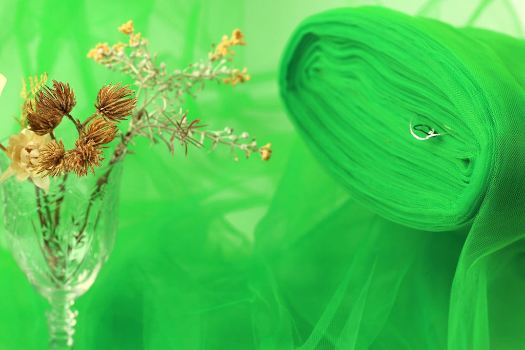 a glass vase filled with dried flowers and a green fabric or material, possibly a piece of tulle, against a green background.