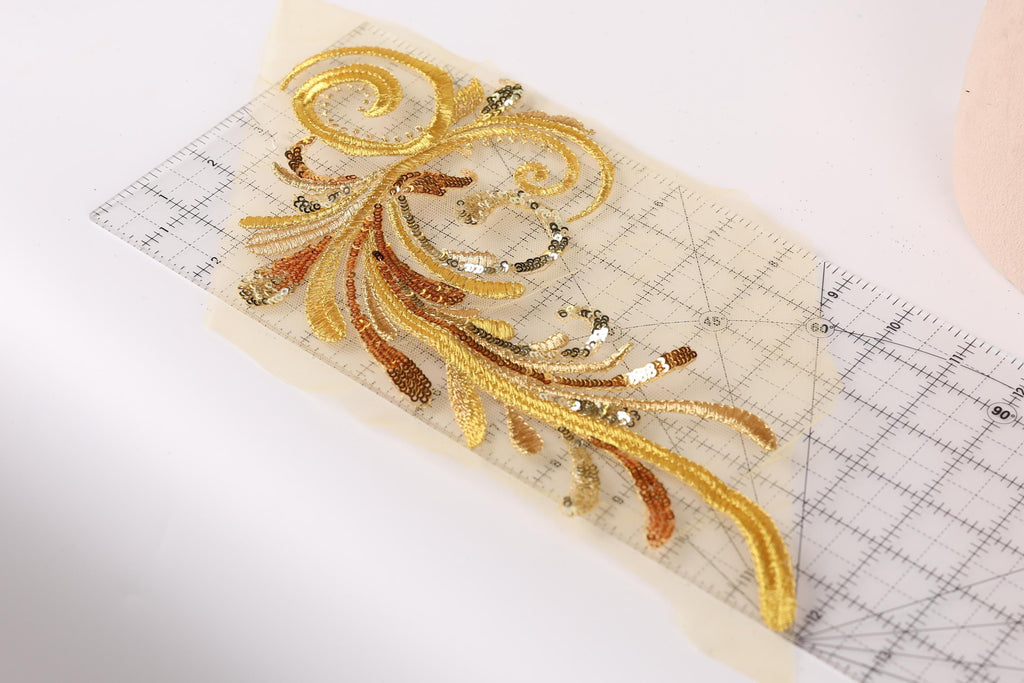 a close-up view of a decorative gold embroidered piece with intricate patterns and designs, placed on a transparent surface.