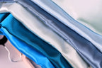 A close-up view of a pile of various colored satin fabric, including shades of blue, white, and gray.