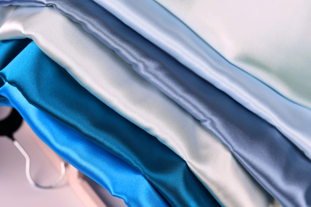 A close-up view of a pile of various colored satin fabric, including shades of blue, white, and gray.