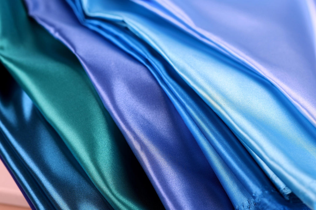 A close-up image of various colored satin fabrics, including blue, green, and purple, arranged in a visually appealing manner.