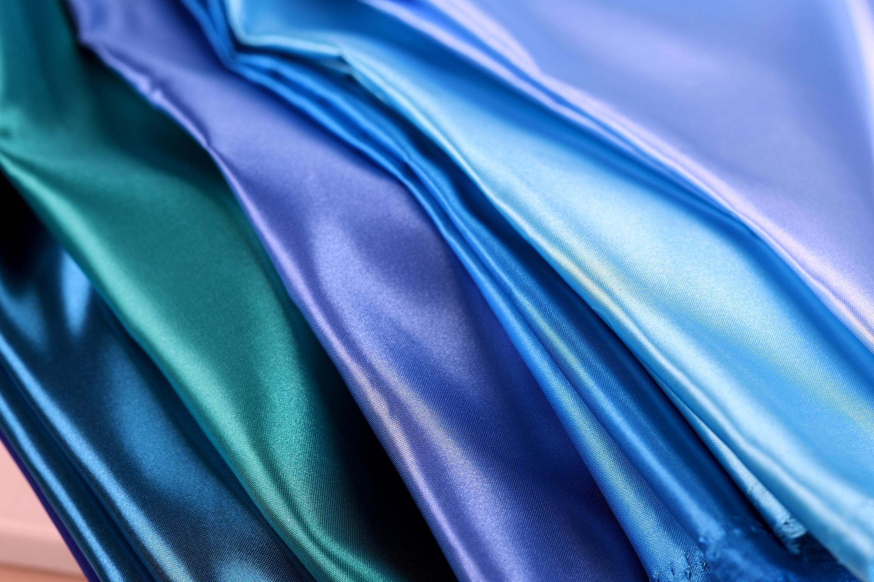A close-up image of various colored satin fabrics, including blue, green, and purple, arranged in a visually appealing manner.