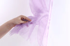 A hand is holding a piece of purple tulle fabric against a white background.