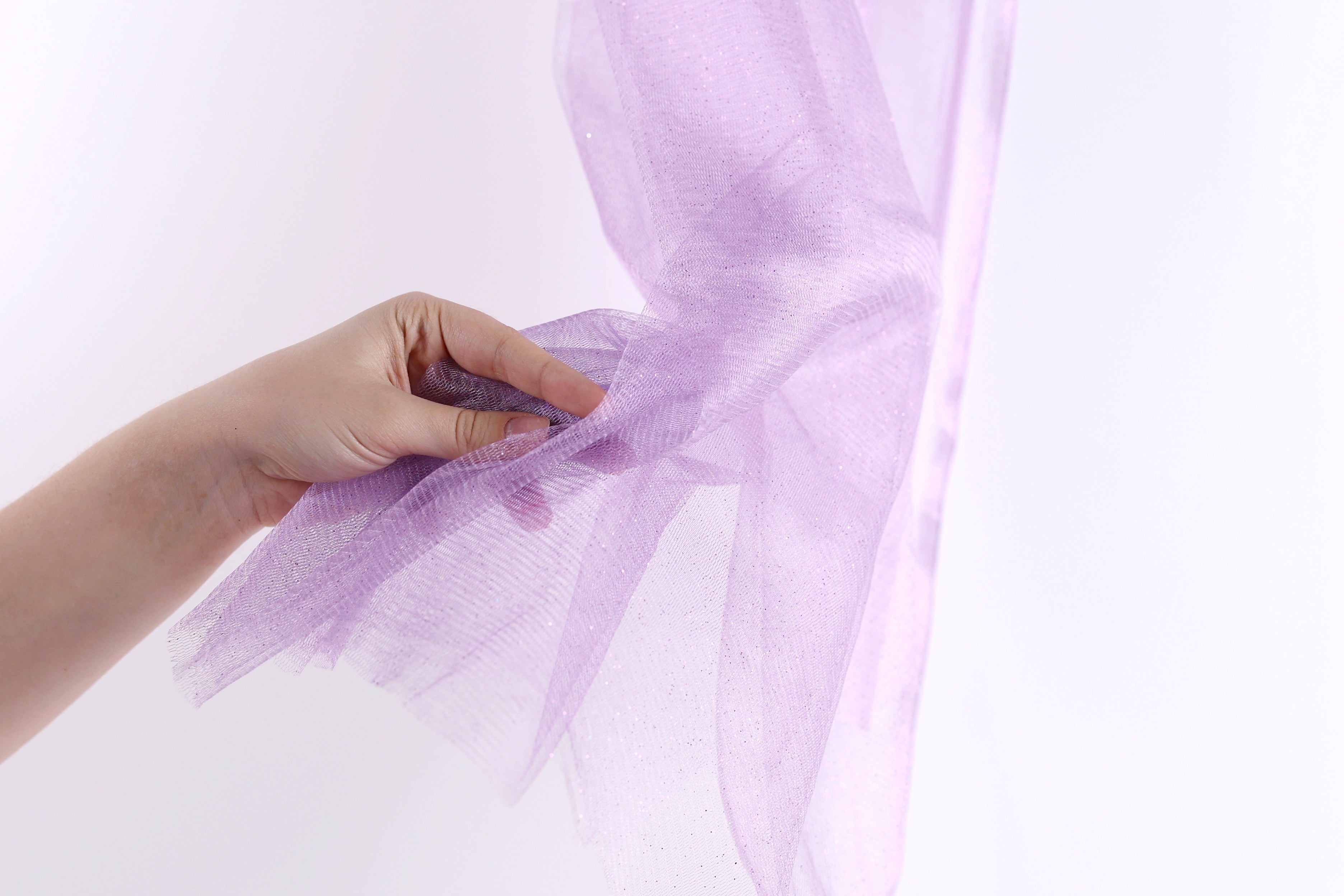 A hand is holding a piece of purple tulle fabric against a white background.