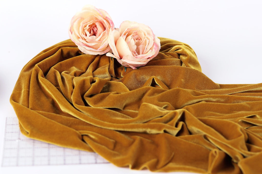 two pink roses resting on a crumpled, golden fabric, which appears to be velvet.