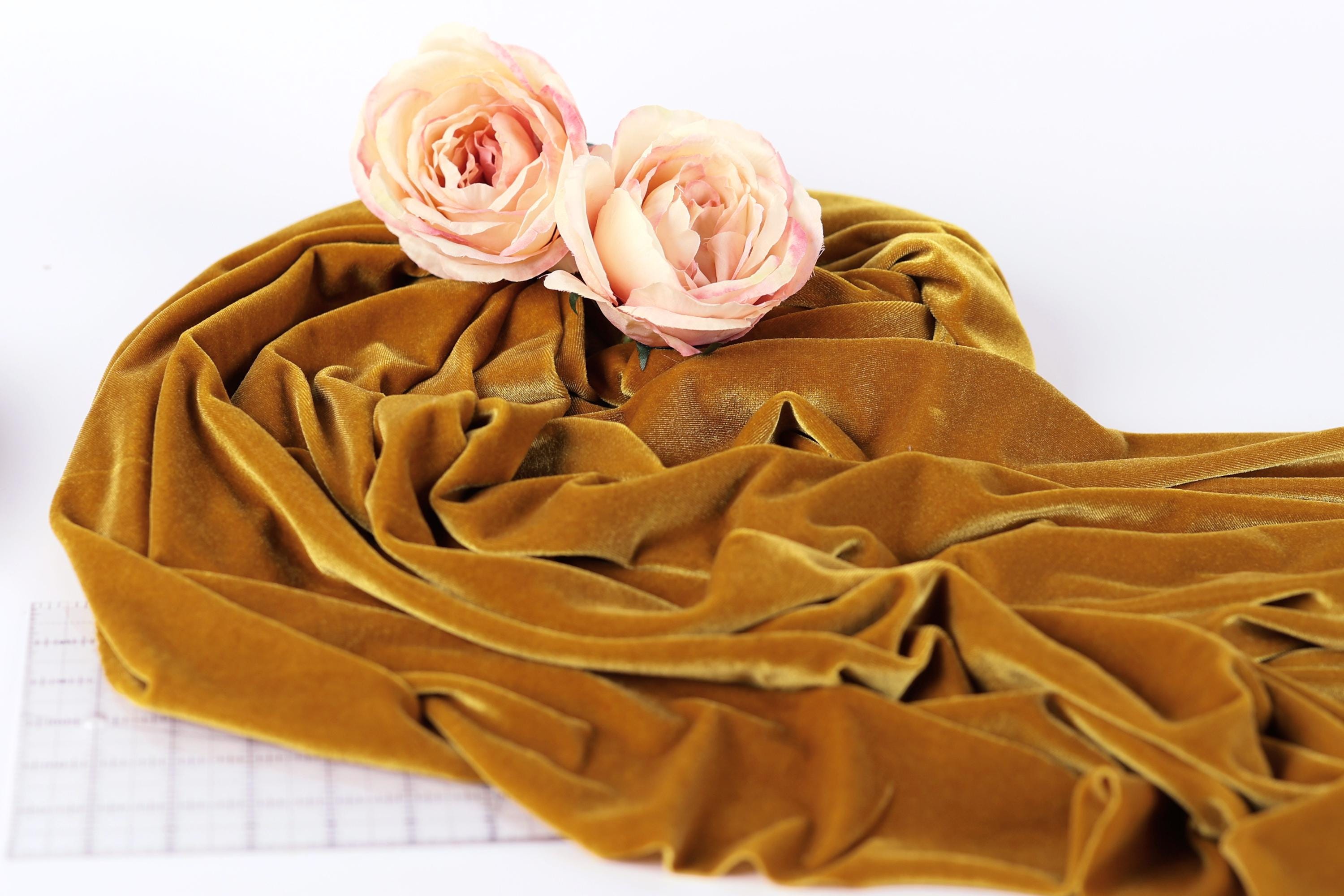 two pink roses resting on a crumpled, golden fabric, which appears to be velvet.