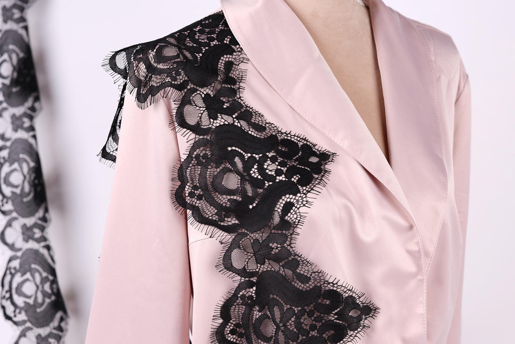 A close-up of a woman wearing a pink blouse with black lace detailing on the shoulder.