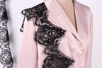 A close-up of a woman wearing a pink blouse with black lace detailing on the shoulder.