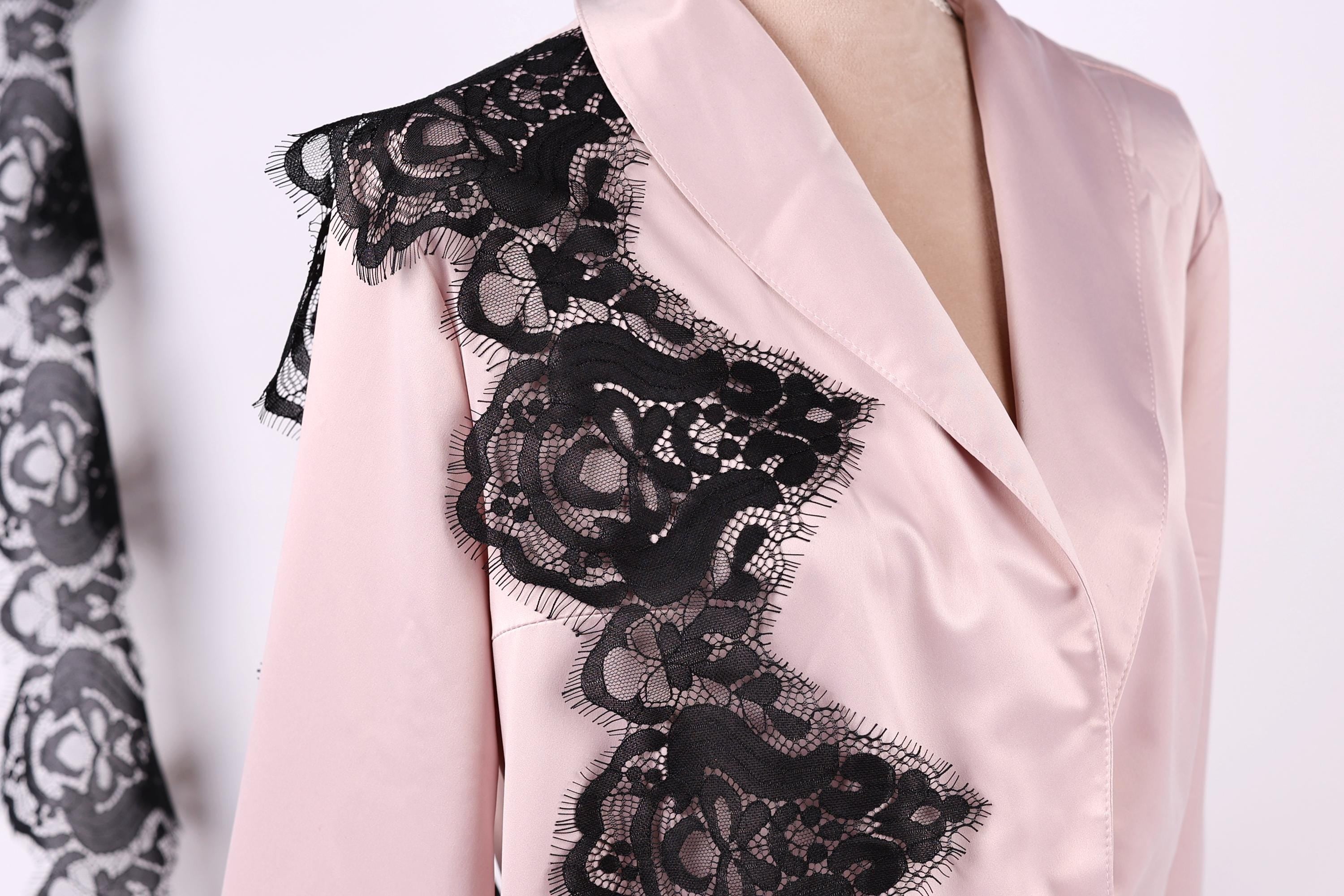 A close-up of a woman wearing a pink blouse with black lace detailing on the shoulder.