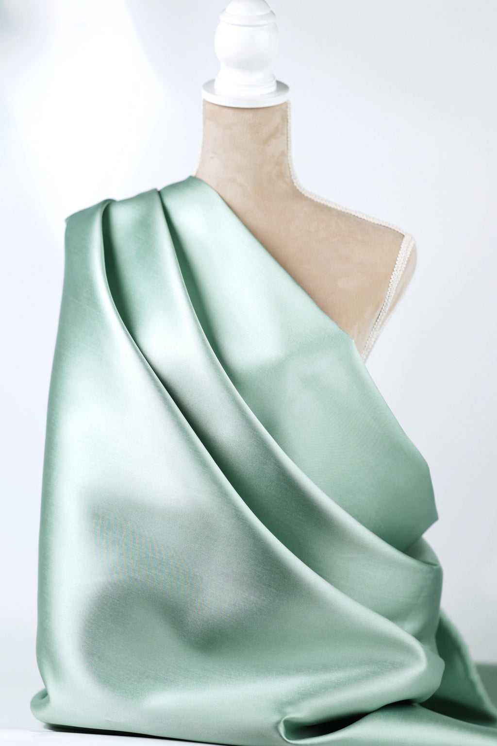 A mannequin is wearing a flowing, mint green satin fabric draped over its body.
