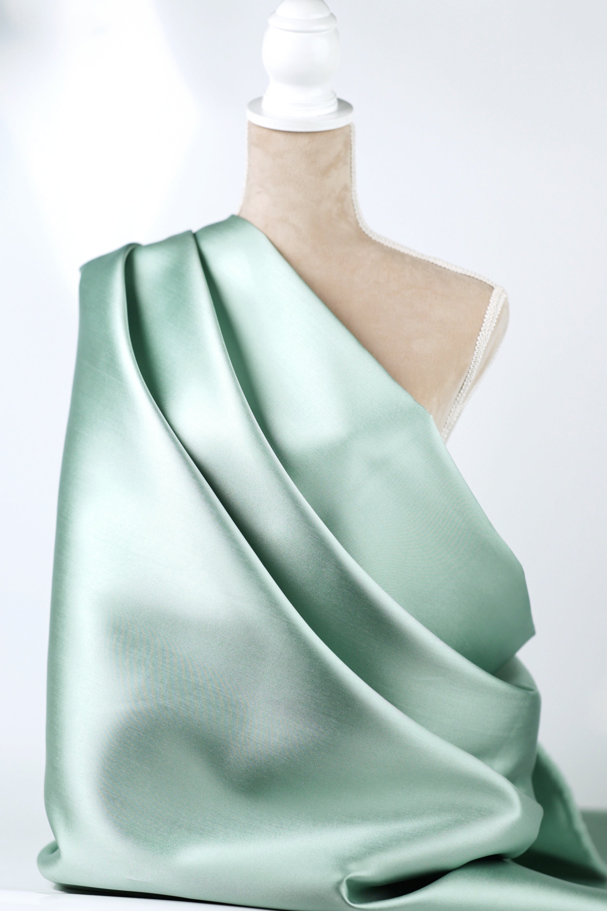 A mannequin is wearing a flowing, mint green satin fabric draped over its body.
