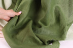 A hand is holding a piece of green fabric, which appears to be a type of linen or cotton material.