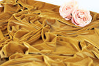 a close-up view of a crumpled, golden fabric with two delicate pink roses resting on top of it.