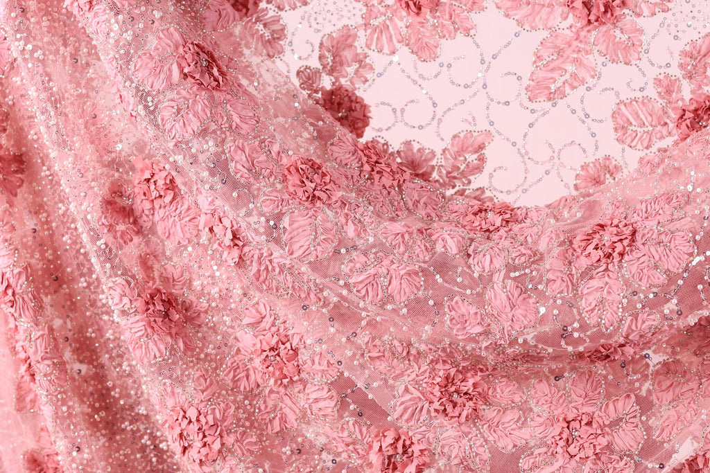 a close-up view of a delicate, pink lace fabric with a floral pattern. The fabric appears to be made of sheer material, giving it a soft and delicate appearance. The lace is intricately designed with pink flowers and leaves, creating a visually appealing and elegant design.
