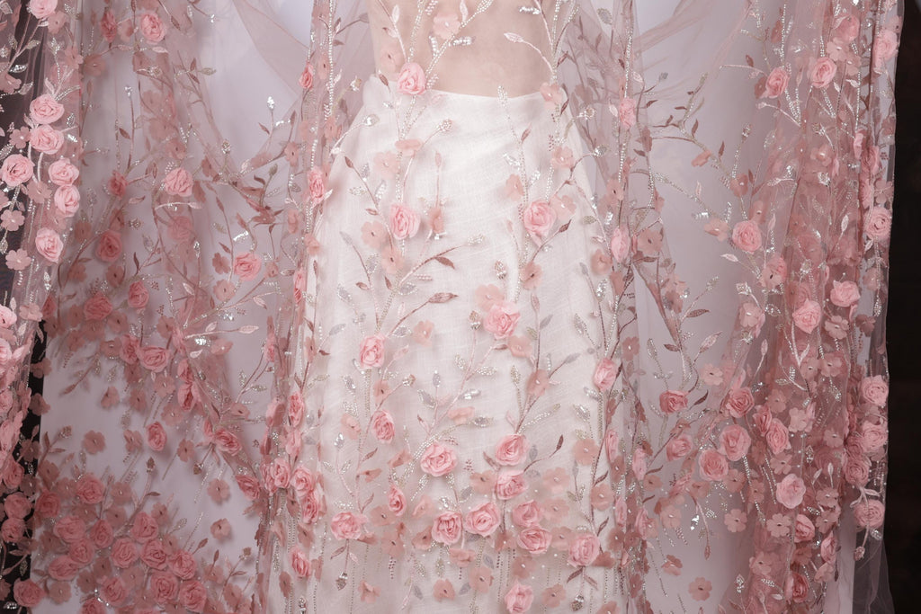 a close-up view of a delicate, sheer fabric with a floral pattern of pink roses. The fabric appears to be a sheer white dress or garment, with the pink roses adding a touch of elegance and softness to the overall design.