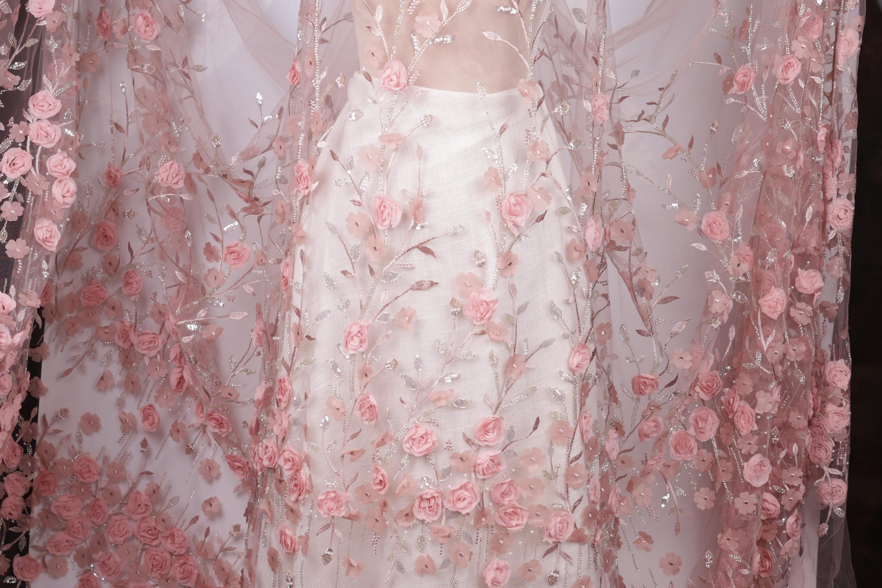 a close-up view of a delicate, sheer fabric with a floral pattern of pink roses. The fabric appears to be a sheer white dress or garment, with the pink roses adding a touch of elegance and softness to the overall design.